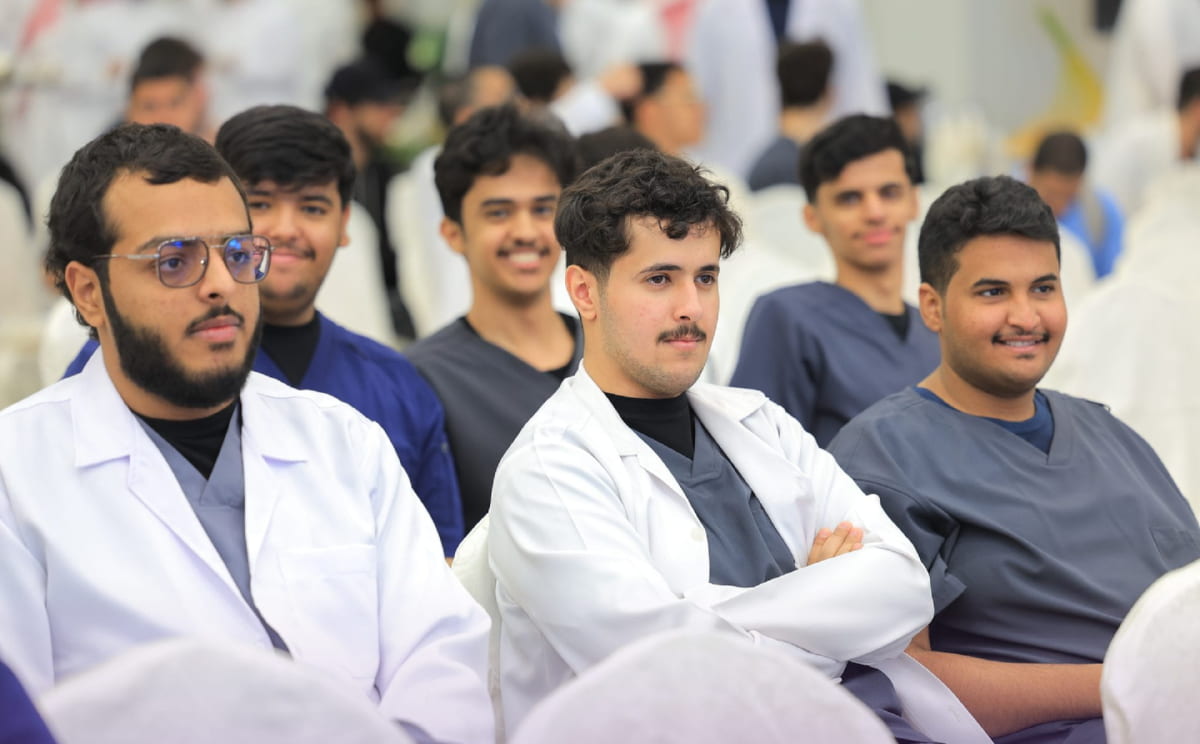 طلبة بمعاطف بيضاء يتابعون فقرات حفل استقبال المستجدّين