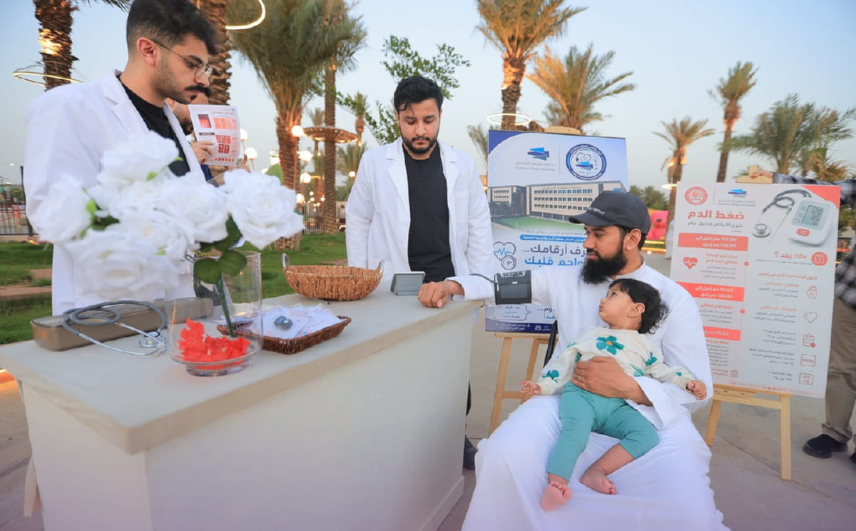 طلبة بمعاطف بيضاء يقيسون ضغط الدم لزائرٍ يحمل طفلته